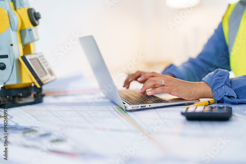 Female Engineer analyzes construction plans using a laptop and surveying equipment in an office setting
