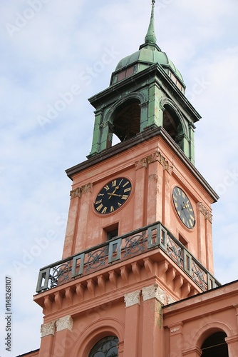 close-up of a pink church tower with large clock and bells