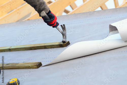 Roofer installing roofing waterproof membrane underlayment using nails and tools on a construction site at daytime