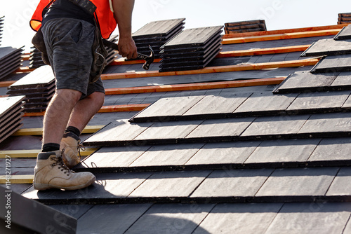 Roofer installs slate roof tiles on a residential building during sunny weather in the afternoon