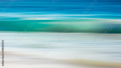 A blurry image of a wave in the ocean. The wave is blue and white. The water is calm and the sky is clear