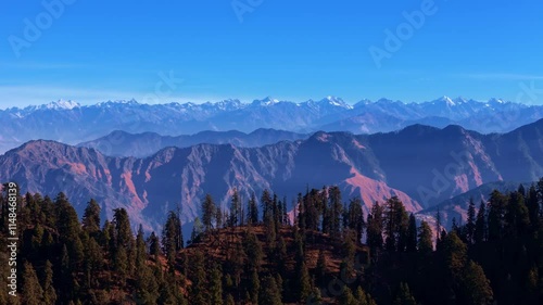 Drone footage of rugged forested hills with reddish mountain slopes under clear blue skies, perfect for nature visuals