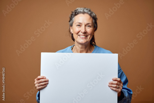 An advertisement studio template portrait photo of a person: an older woman with a warm smile on her face, holding a blank white sign in front of her.