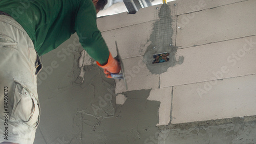 The walls of the house are drilled into embedded blocks for installing air conditioners. A male worker is plastering lightweight bricks with cement. Concept of working in a construction site