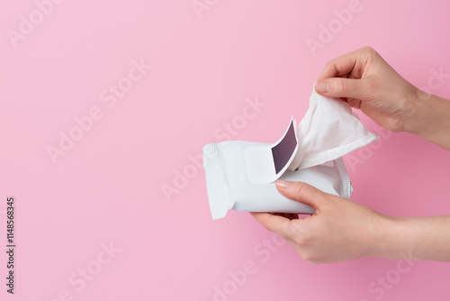 Woman taking wet wipe from pack on pastel pink background. An open pack of hand and body wet wipes in woman hands. Concept of hygiene and beauty