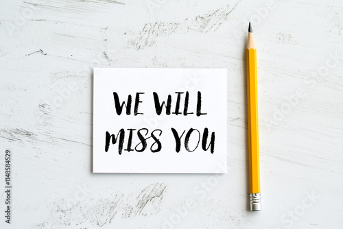 We will miss you message written on a white card with pencil. Conceptual we will miss you symbol. Copy space. photo