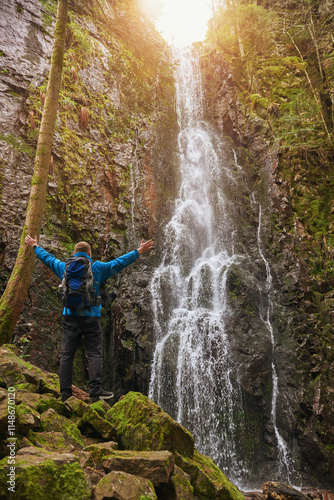 Tourist attraction of Germany - falls of Burgbach Waterfall near Schapbach, Black Forest, Baden-Wurttemberg, Germany. Man hiker in blue jacket standing on stone and looks at flow of falling water