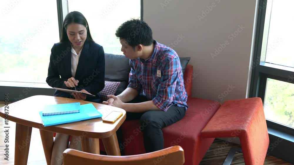 A woman and a man are sitting at a table with a tablet in front of them. Scene is friendly and collaborative A woman and a man are sitting at a table with a tablet in front of them. Scene is friendly and collaborative