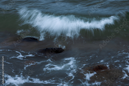 Blurred crest of the sea wave among the boulders near the shore