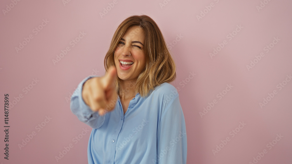 Blonde woman winking and pointing directly at the camera over a pink background in a playful manner, wearing a casual blue shirt, creating an inviting and friendly mood. Blonde woman winking and pointing directly at the camera over a pink background in a playful manner, wearing a casual blue shirt, creating an inviting and friendly mood.