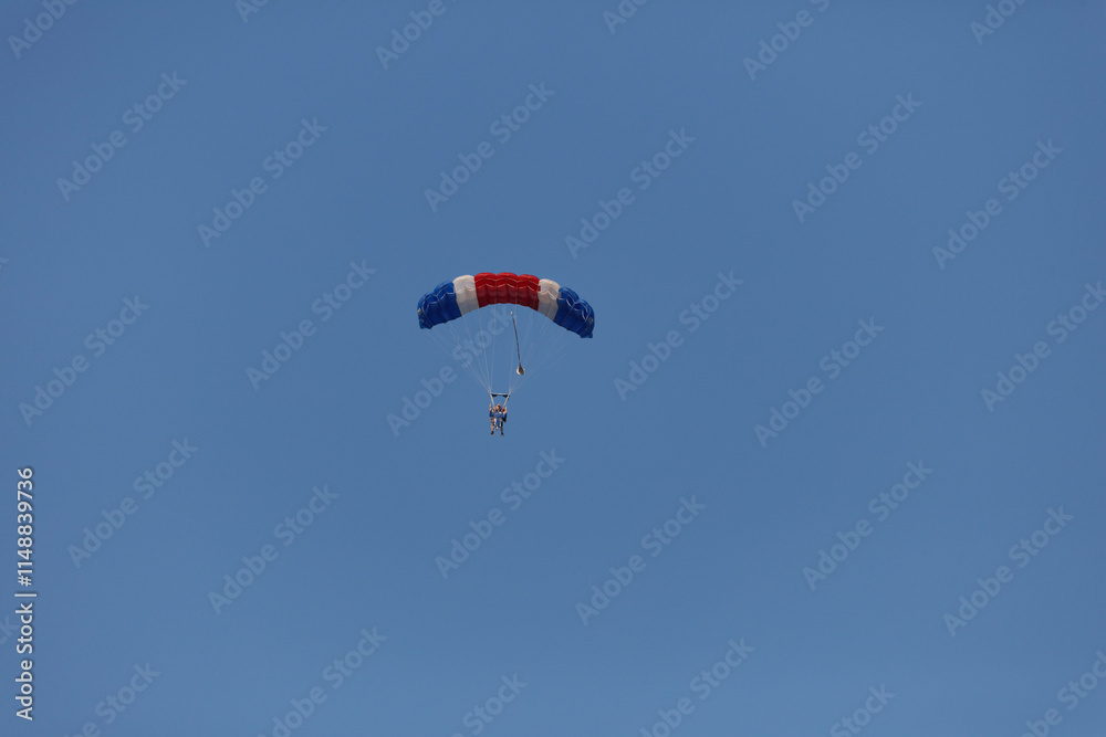 Two people in a red, white, and blue parachute glide through a clear blue sky. Two people in a red, white, and blue parachute glide through a clear blue sky.