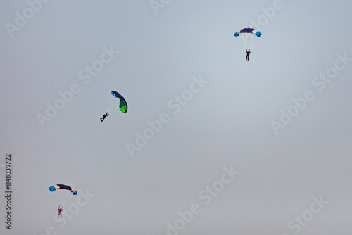 Several skydivers with colorful parachutes descend.  A gray, overcast sky is the backdrop.