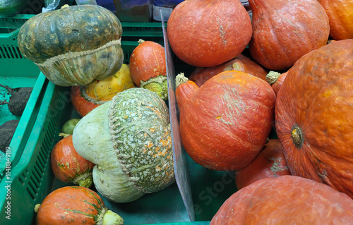 Green and orange small pumpkins are lying in a green container on a shelf in the store photo