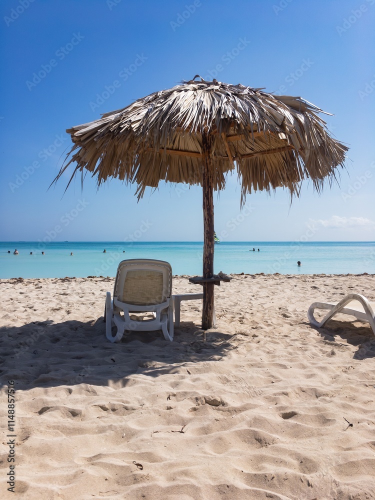 Sand beach, sunbeds, straw umbrellas in Varadero, Cuba with unrecognizable people in sea