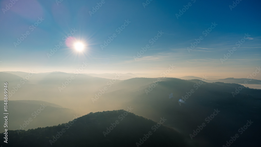 Fototapeta premium Capturing an aerial view of endless mountain ridges disappearing into the fog, illuminated by the bright morning sun at sunrise