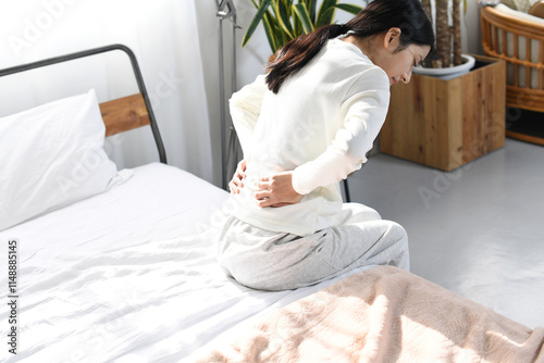 ベッドの上で腰痛や背痛に悩むアジア人女性