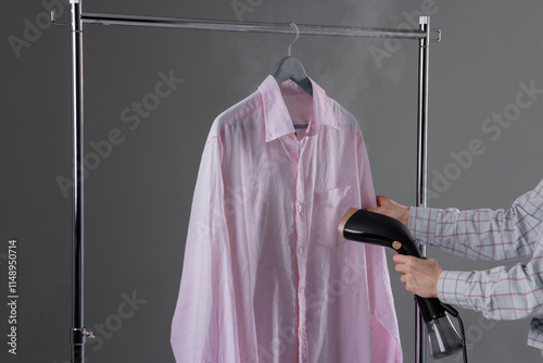 Woman steaming clothes on hanger at home, close up, handheld steamer in woman's hand