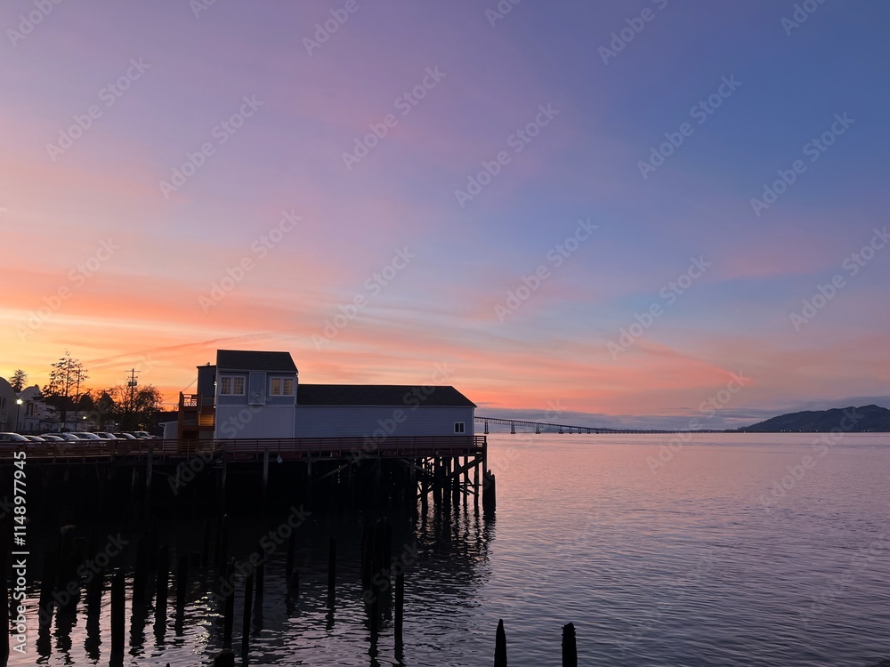 A beautiful sunset in Astoria, Oregon, with a building on stilts above the water, casting a warm glow from the setting sun A beautiful sunset in Astoria, Oregon, with a building on stilts above the water, casting a warm glow from the setting sun