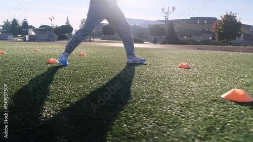 Football player training on a field. Man in light blue hoodie and purple pants, practicing agility drills with orange cones