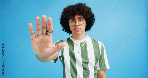 Man, portrait and hand with stop for rejection, no or protest on a blue studio background. Male person, gen z or young model with gesture, sign or objection for refusal, enough or resistance on space