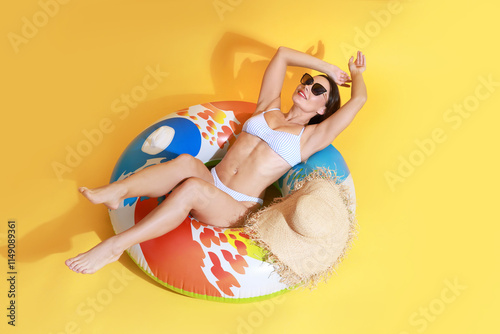Beautiful woman in swimsuit with inflatable ring on yellow background photo