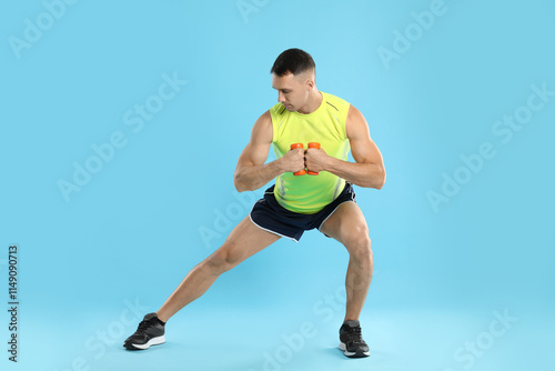 Man exercising with dumbbells on light blue background