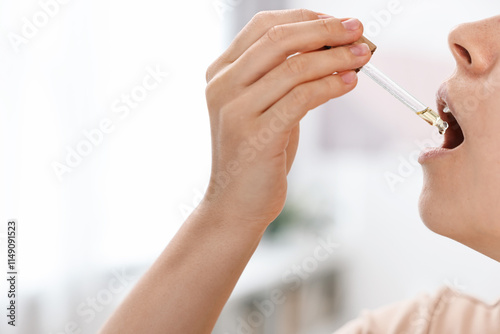 Young woman taking CBD tincture indoors, closeup. Space for text