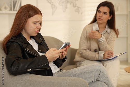 Rebellious teenage girl using smartphone instead of consultation with psychologist in office, selective focus photo