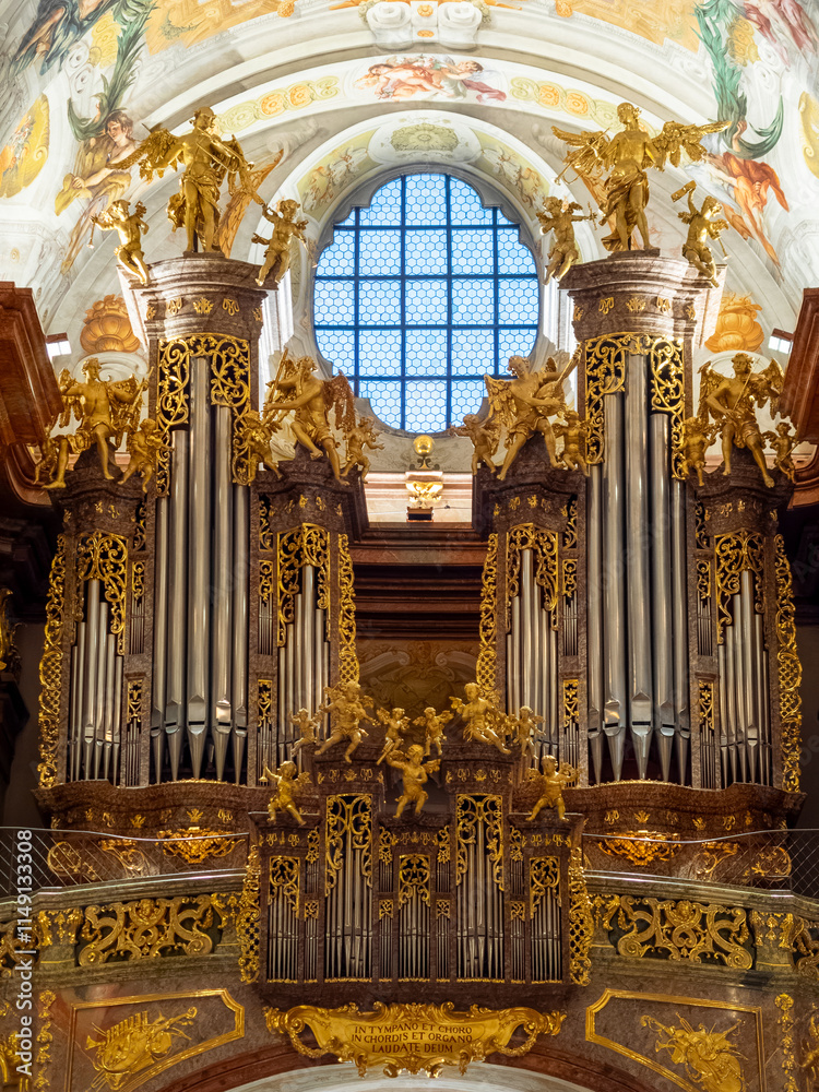 Ornate organ display in a historic church featuring intricate gold detailing and a stained glass window