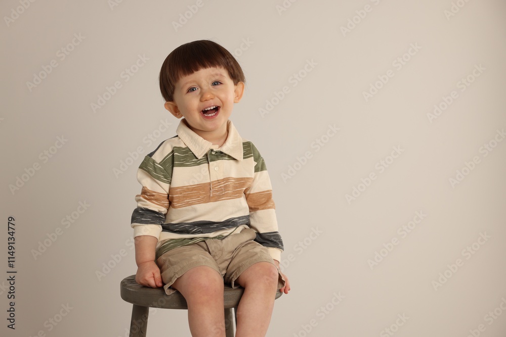 Emotional little boy sitting on stool against light grey background. Space for text Emotional little boy sitting on stool against light grey background. Space for text