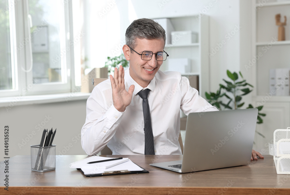 Smiling middle aged man having videochat via laptop at table in office