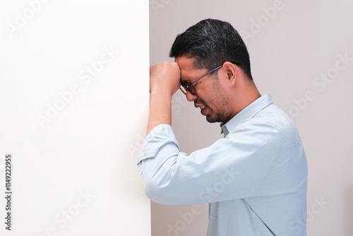 A man put his head on the wall suffering headache