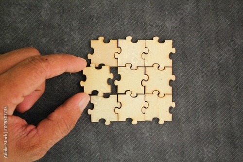 The puzzles are arranged and the hand holds the last puzzle for combination. concept of solution or complete task. teamwork and cooperation concept. Hand to complete last piece wood puzzle. 