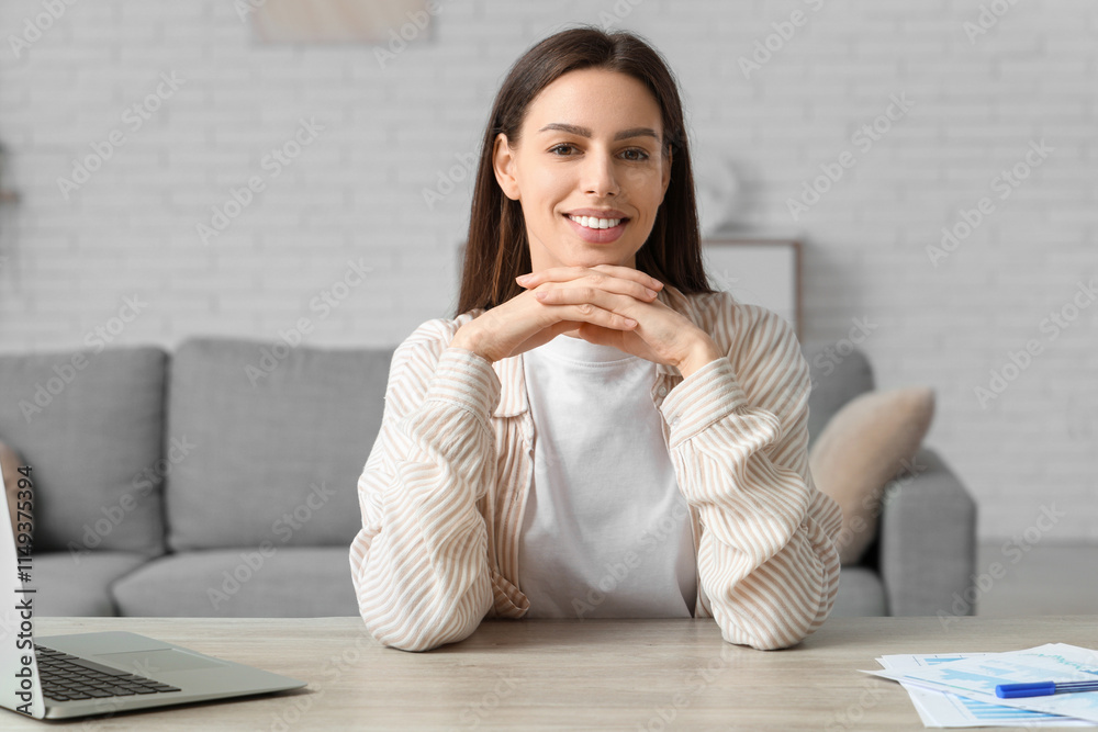 Beautiful young happy woman working with laptop and documents on table at home