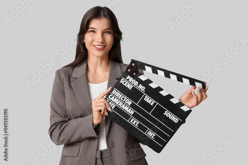 Young happy female film director with movie clapper on grey background