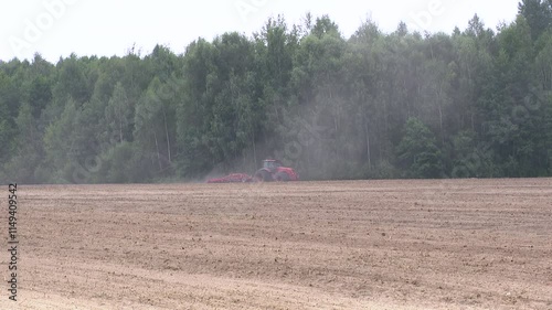 Farmer plowing stubble field with red tractor.  Farmer in tractor preparing land with seedbed cultivator.  Tractor working in the field, preparing the land for planting, working plowed field
