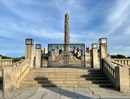 The entrance to Monolitten in Vigeland Park, Oslo, featuring a majestic wrought-iron gate with intricate designs, leading to the iconic sculpture surrounded by greenery. photo