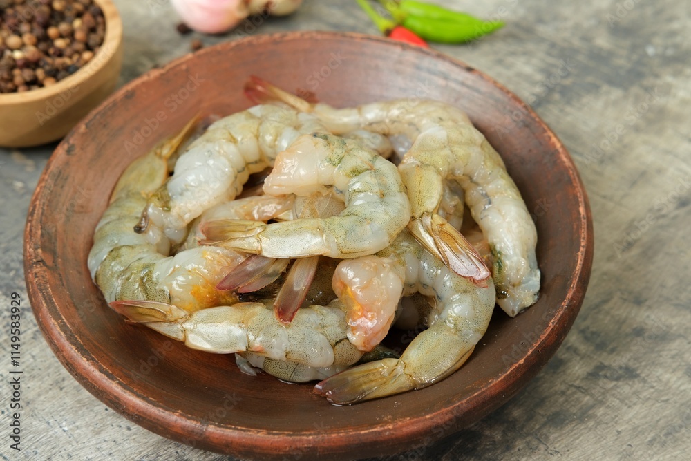 Raw peeled shrimp neatly arranged on a wooden plate with spices like garlic, chili, pepper, and shallots on a white tile background. Perfect for cooking preparation or seafood-themed content. Raw peeled shrimp neatly arranged on a wooden plate with spices like garlic, chili, pepper, and shallots on a white tile background. Perfect for cooking preparation or seafood-themed content.