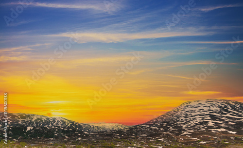 Mountain landscape with peaks covered with melted snow. Aerial view of snow covered mountains in summer during sunset