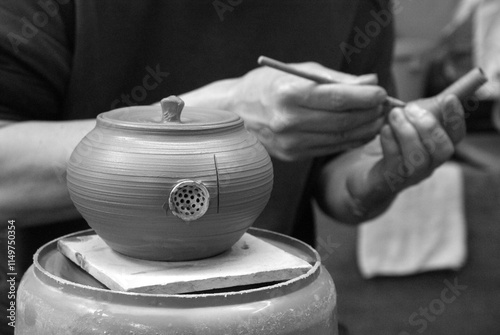 A potter adds fine details to a clay teapot 