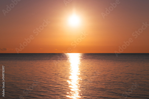 A breathtaking view of the sun setting over the horizon, casting a golden glow on the calm ocean waters. 