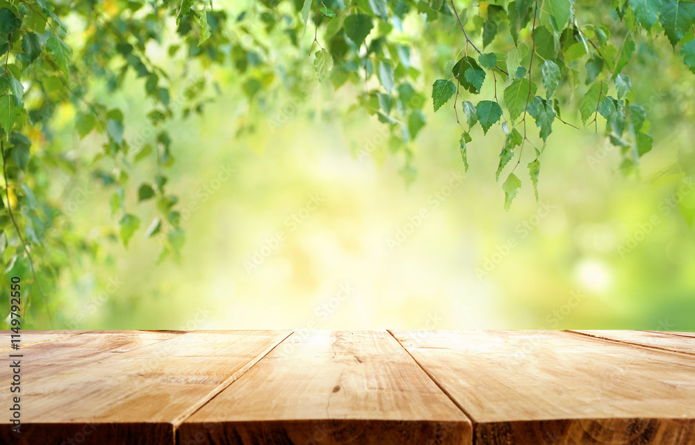 Beautiful natural spring background with green juicy young foliage birch and empty wooden table in nature outdoor.