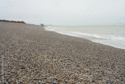 Rocky beach stretches along a calm shoreline under a cloudy sky in an expansive natural landscape
