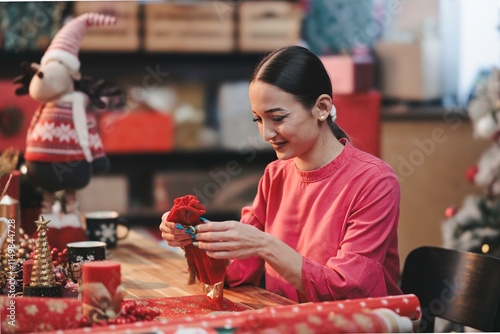 In a cozy room adorned with festive decor, a woman enjoys a crafting session, meticulously creating Christmas decorations. She smiles as she works, surrounded by cheerful holiday elements photo