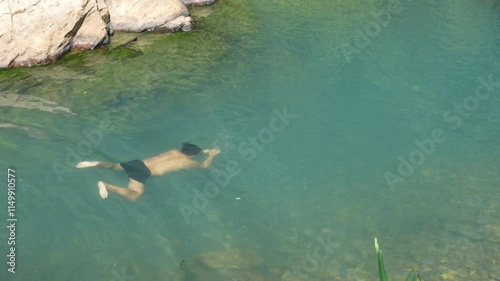 Young Asian man travel nature on summer holiday vacation relax and enjoy outdoor lifestyle relaxing and swimming at waterfall lagoon at forest mountain