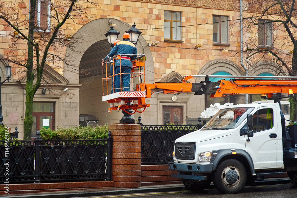 Aerial platform truck with electricians in lift bucket replacing led light bulbs during street lamp maintenance and repair work. Workers in cherry picker repairing streetlights, replacing led bulbs