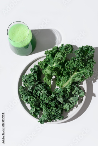 Batido de jugo de col rizada verde y hojas frescas de col rizada en un plato blanco sobre fondo blanco. Vista superior photo