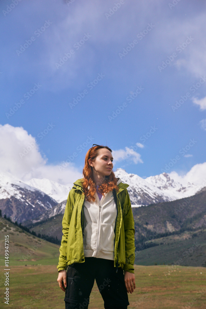 Naklejka premium A young girl in bright clothes smiles against the background of snowy peaks in a mountain valley