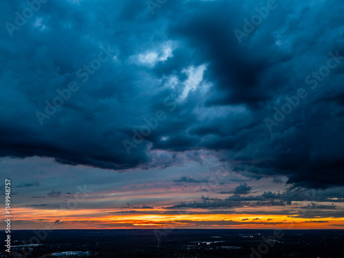 Stormy Sunset Drama. Intense dark clouds dominate the sky while a vibrant orange and yellow sunset glows on the horizon, creating a contrast of moody and serene tones.