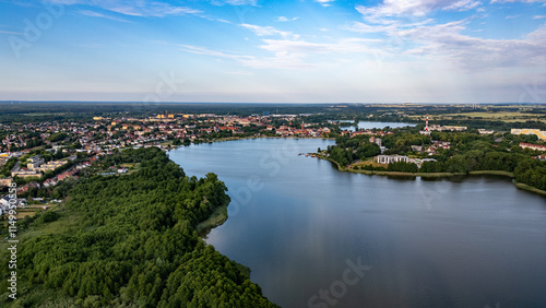 Wallpaper Mural Panoramic View of Lake Raduń in Wałcz, Poland. Aerial view of Lake Raduń in Wałcz, Poland, surrounded by lush greenery, urban architecture, and a serene water surface reflecting the clear blue sky. Torontodigital.ca